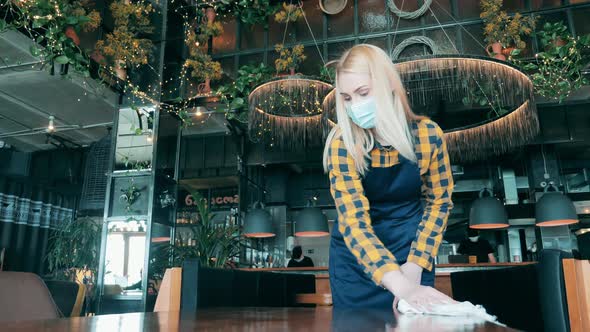 Blond Waitress is Wiping a Table While Wearing a Mask