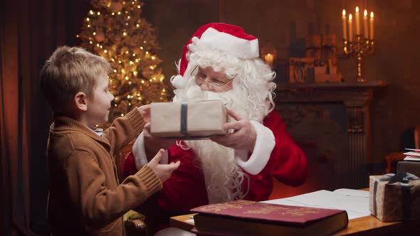 Santa Claus and little boy. Cheerful Santa is working at the table. Christmas concept.