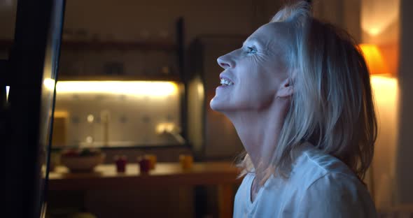 Side View of Smiling Aged Woman Applauding Watching Tv Show Late in Evening