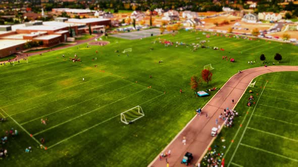 Teams playing football on various fields in a park or school yard - tilt shift effect on aerial hype