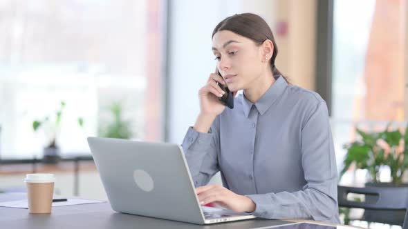 Young Latin Woman Talking on Smartphone While Using Laptop