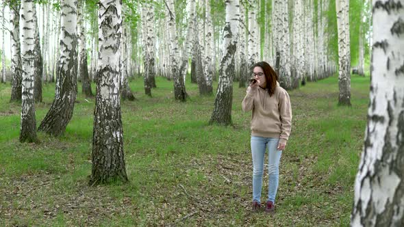 A Young Woman Is Looking for a Cellular Network in a Birch Forest. A Girl Is Talking on the Phone