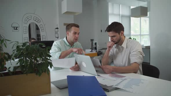 Pair of Marketer Looking on Graphs and Charts Discussing Results of Sales