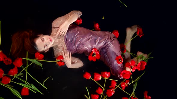 Sexy Red Haired Woman is Floating in Black Water Red Tulips Around Her Passion and Seduction