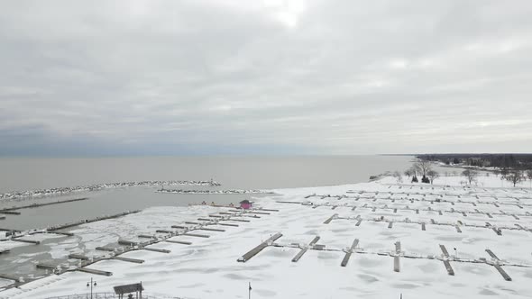 Aerial view over Lake Michigan marina covered in snow and ice. Cloudy sky and forest seen.