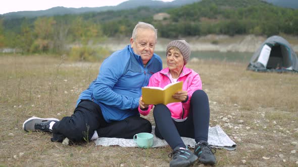 Happy Senior Couple Reading a Book While Camping in the Woods  Elderly Travel Lifestyle