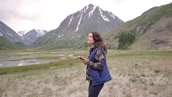 Woman Tourist in Headphones Dancing on a Background of Mountains and Scenery. Tourist Trip