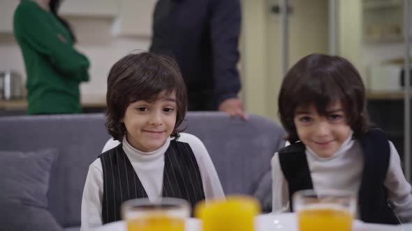 Cute Middle Eastern Twin Brothers Sitting at Table with Couple of Unrecognizable Parents at