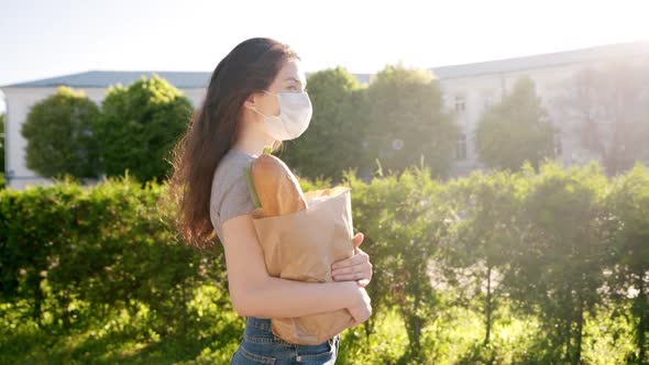 Caucasian Young Pretty Woman Delivery Worker in Medical Mask Walking the Street and Carrying Packet