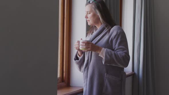 Woman drinking coffee while looking out of the window at home