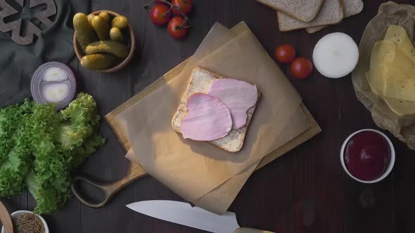 Flat Lay of the Sandwich with Sliced Ham and Vegetables on the Wooden Board in the Beam of Light