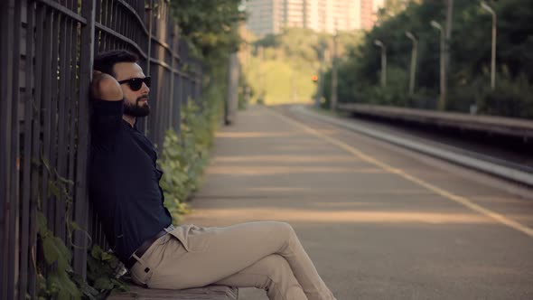 Businessman Relaxing And Sitting On Railway Train Station Platform. Man Passenger Wait Tram.