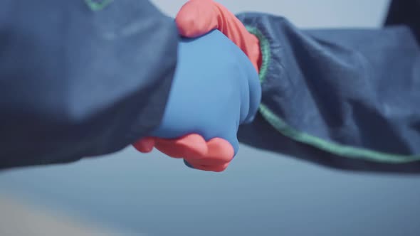 Close-up Handshake of People in Chemical Suits and Protective Gloves. Two Unrecognizable Workers