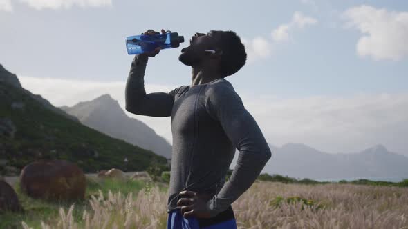 African american man drinking water from bottle while hiking in the mountains