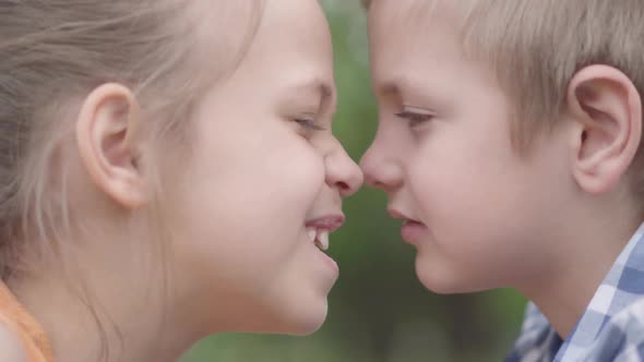 Close-up Face of Adorable Boy and Girl Sitting in the Park, Trying To Rub Their Noses and Having Fun