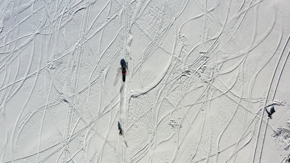 Snowmobile towing skier, top down tracking aerial view. Winter snow fun on sunny day, high angle dro