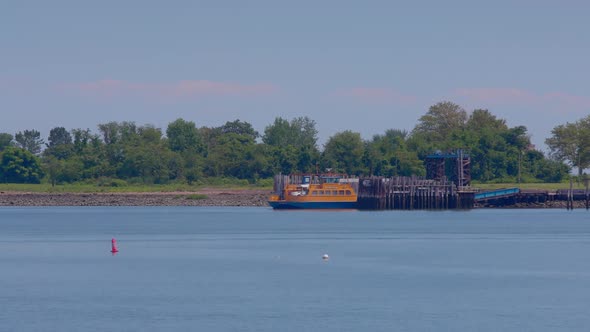 Orange Roll-on, roll-off ferry leaving the prison dock at Hart Island, with white prison bus. Blue s