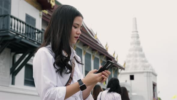 Young Asian females using a smartphone while standing on the street beside Wat Phra Kaew in Thailand