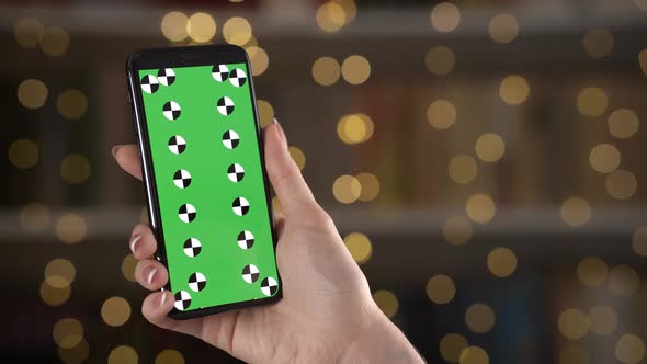 Phone with Greenscreen in Hands of Lady Who Scrolls and Taps on Screen Bokeh Background