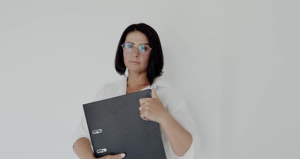 Portrait of Teacher with Glasses and Big Black Folder in Hands Looking at Camera