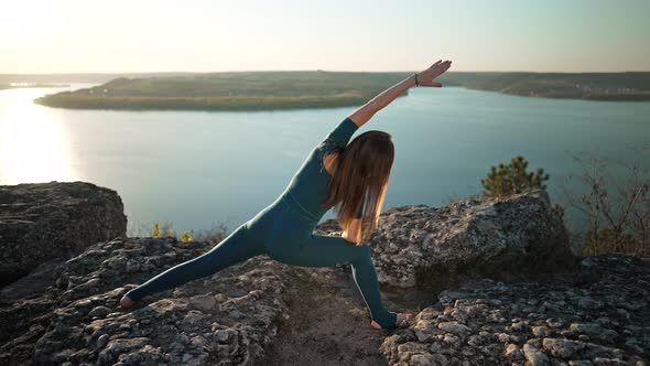 Sporty Woman in Blue Costume Practicing Yoga on High Rock Above Water