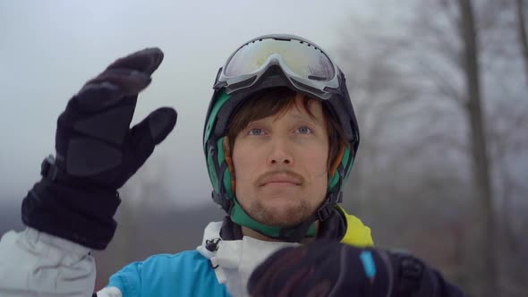 Closeup Shot of a Young Man Wearing a Helmet with a Snowboard in a Mountain Resort. He Puts on His