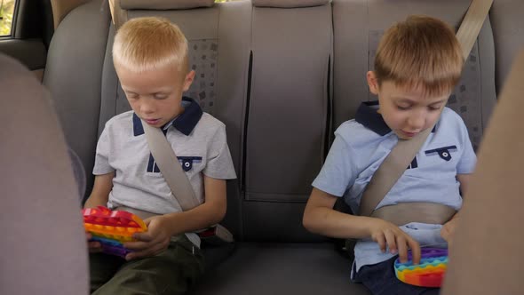 Two Little Brothers are Sitting in the Car and Playing an Antistress Toy Pop It