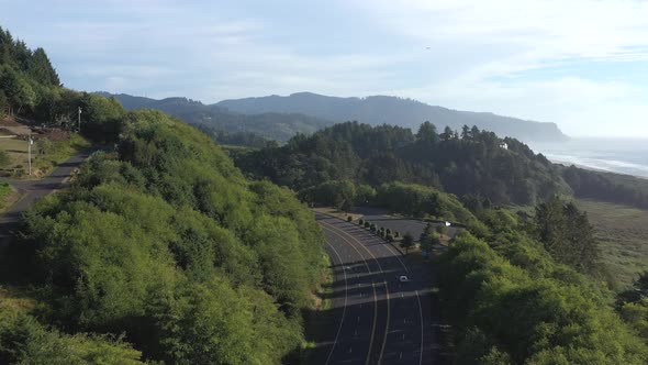 Following a car driving on a scenic road next to the beach in Oregon as a bird flies in the air.