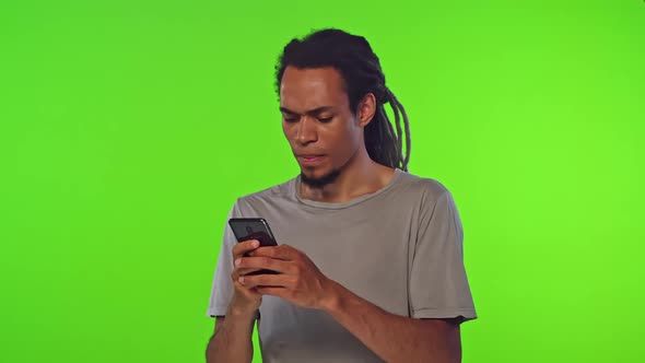 Young Fussy African American Man Typing Message on Phone Stands on Studio