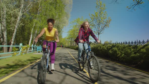 Lovely Multiethnic Females Riding on Bicycles in Public Park