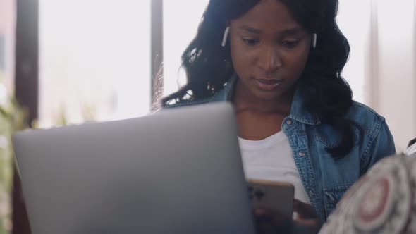 Concentrated African woman wearing earbuds texting on phone