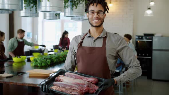 Portrait of Handsome Afro-American Guy Holding Roasting Pan with Meat in Cooking School