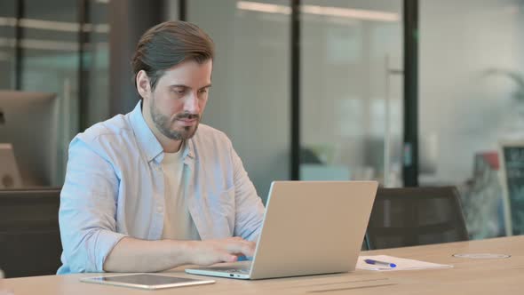 Mature Adult Man with Laptop Pointing at Camera in Office