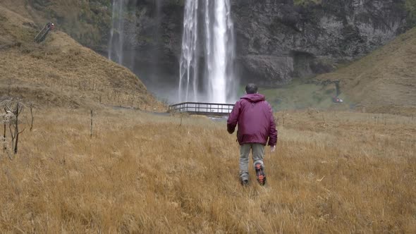 Carefree traveling man running towards waterfall