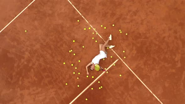 Portrait of smiling girl relaxing on tennis court with a lot of balls and racket after hard