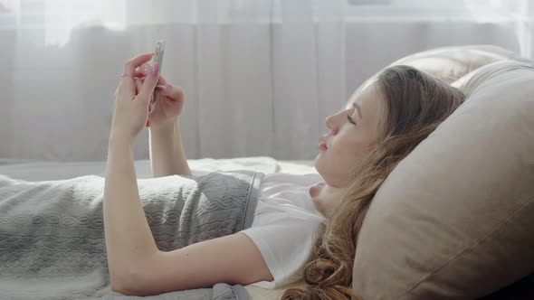 Young Woman Laying On Bed And Using Social Media