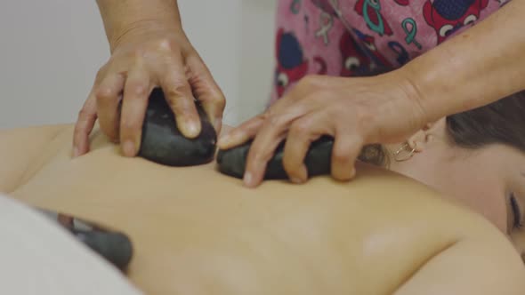 Masseuse Giving a Massage To Female's Back Using Stones