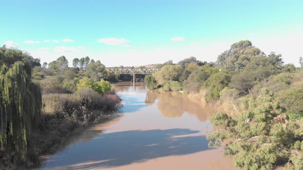 aerial shot flying close to the water towards an old rusty bridge in the background