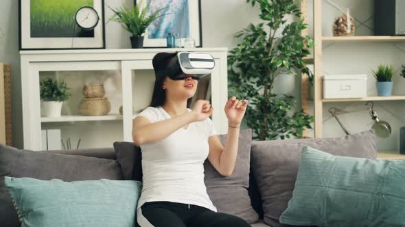 Smiling Young Lady in Augmented Reality Glasses Is Moving Hands and Turning Head Sitting on Sofa at