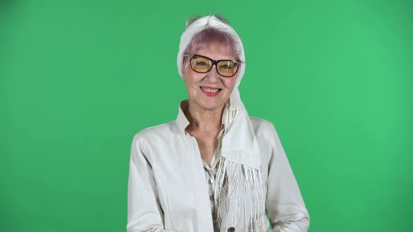 Portrait of Old Stylish Woman Is Looking Straight and Smiling Isolated Over Green Background