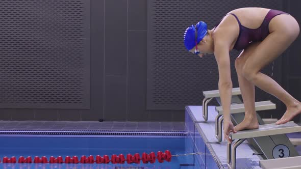 Young Woman Swimmer Stands on the Stand and Dives in the Pool