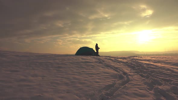 Hiker eating in front of tent, at sunset, in snowy winter mountains