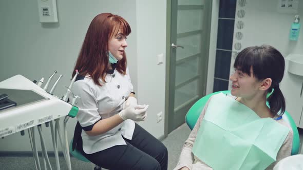 Female doctor explains her patient how to look after the teeth on the background of dental room