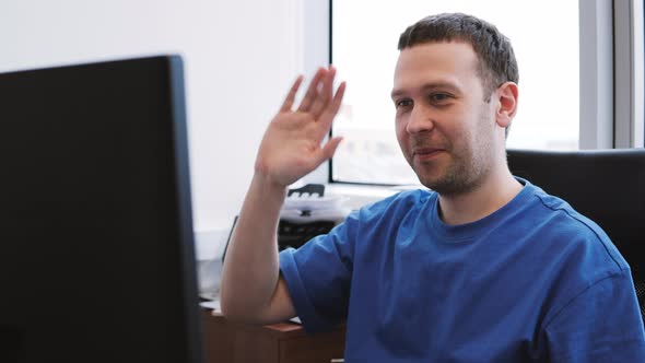 Man in Blue Tshirt Makes Video Call on Desktop PC While Sits on Chair in Office