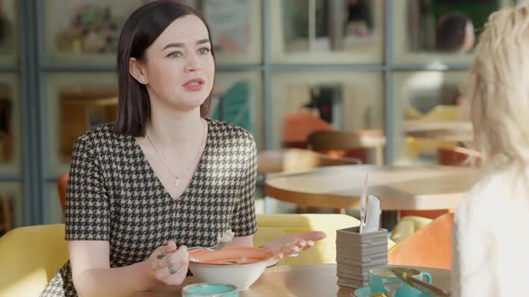 Portrait of Young Confident Woman Talking with Friend and Eating in Restaurant