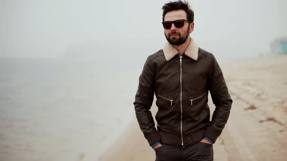 Man Walking On City Beach In Foggy Day. Guy In Sunglasses Walks On Sand.  Man Walking On Sand Beach.