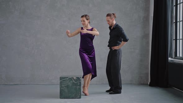 Man Teaching Woman Dancing Tango in Grey Studio Against Large Windows