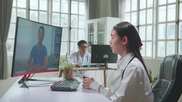 Woman Doctor Having Video Conference On Computer In Workplace With Man Patient On Screen Display