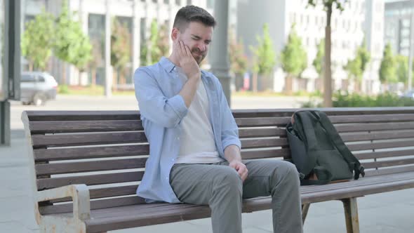 Young Man with Toothache Sitting on Bench