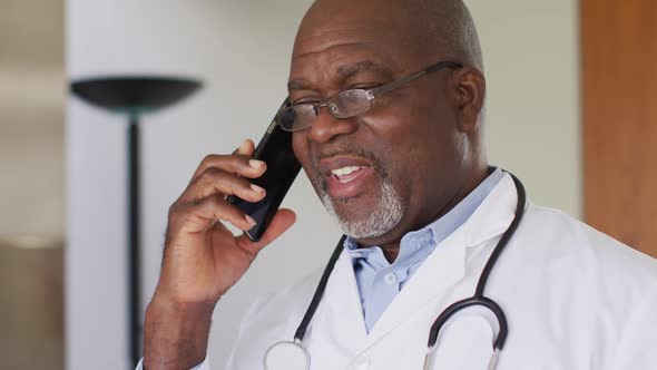 African american senior male doctor wearing white coat talking on smartphone